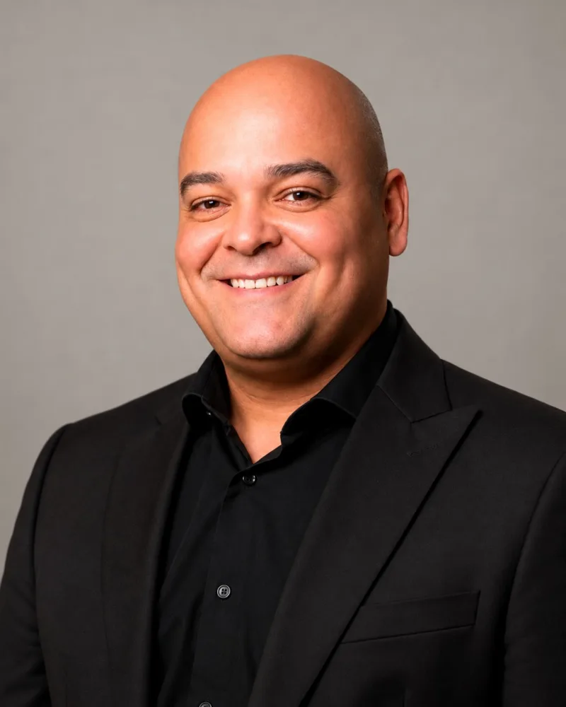 Retrato de Wagner da Mota Mendonça, de terno e camisa pretos, sorrindo diante de fundo cinza